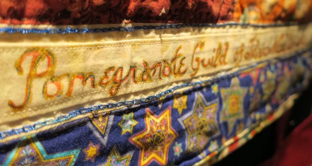 An image of an embroidered cloth that reads "Pomegranate Guild"