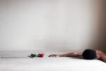 A person lying on a bed reaching towards a single rose, emphasizing themes of longing and tenderness.