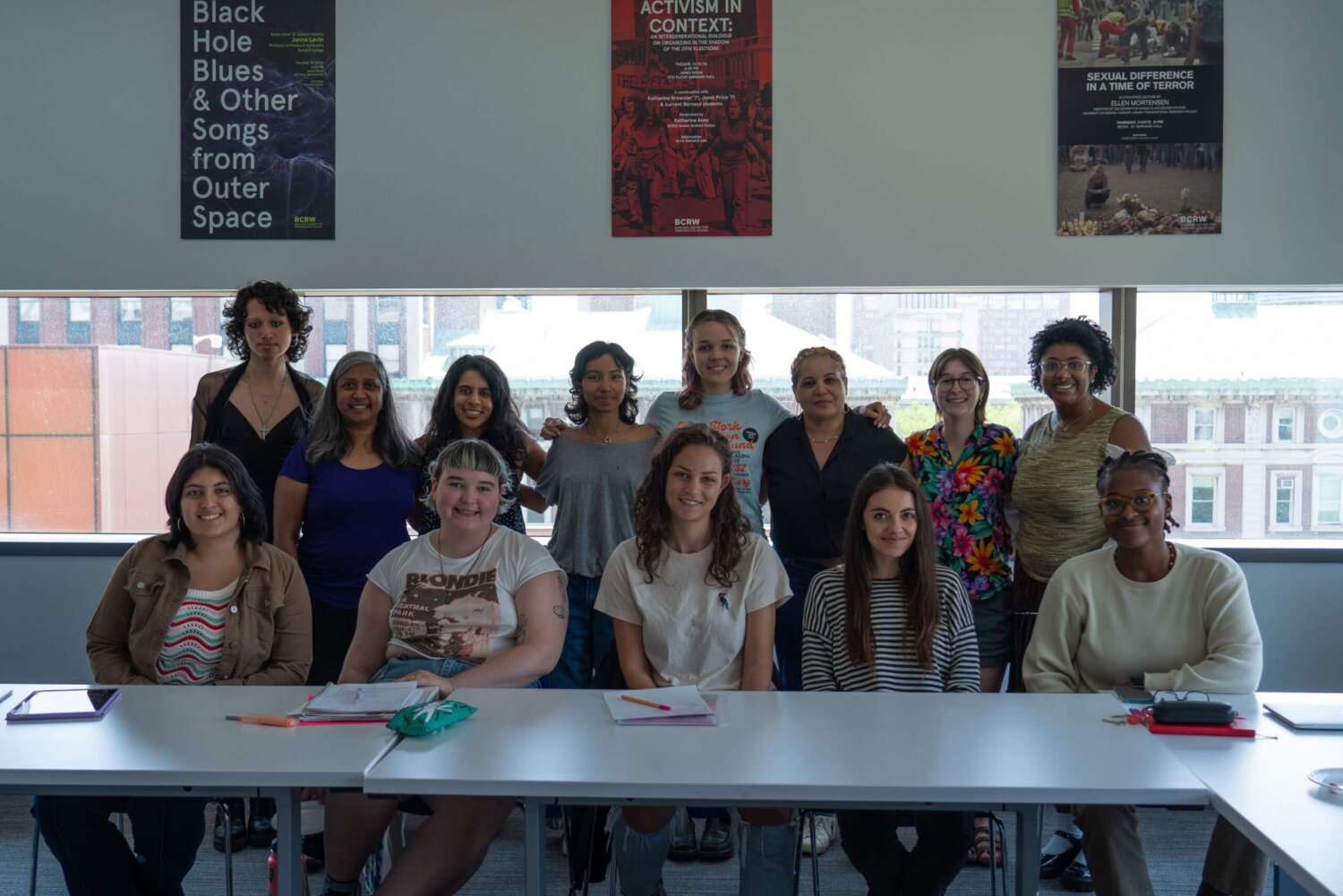 Group of women smiling, posing in a bright, urban classroom with posters on the wall.