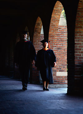 two professors in academic regalia walk on a university campus