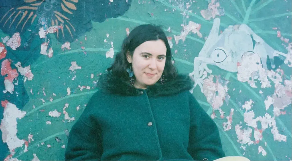 Young woman smiling against vibrant, nature-inspired graffiti art at Barnard.